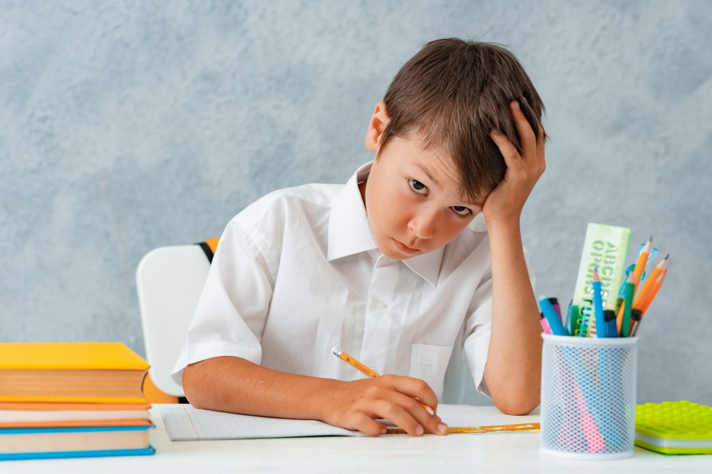 Back to school. Happy smiling student draws at the Desk. A schoolboy solves his homework. A boy from elementary school